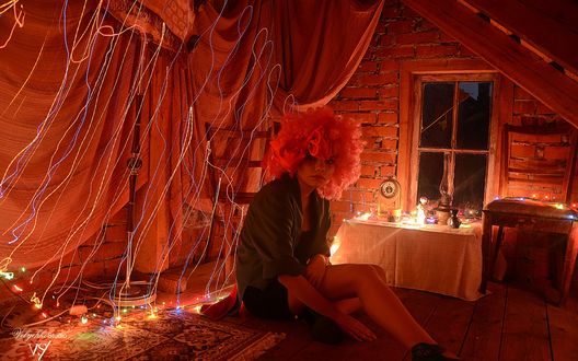 Обои на рабочий стол Грустная, плачущая, одинокая девочка с взлохмаченными, светлыми волосами, сидящая возле ковра, на полу, на чердаке в окружении светящихся, праздничных гирлянд, лежащих на полу и на стуле