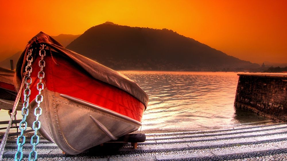 Обои для рабочего стола Лодка, прикованная цепями к берегу горного озера на фоне рассвета на утреннем небосклоне