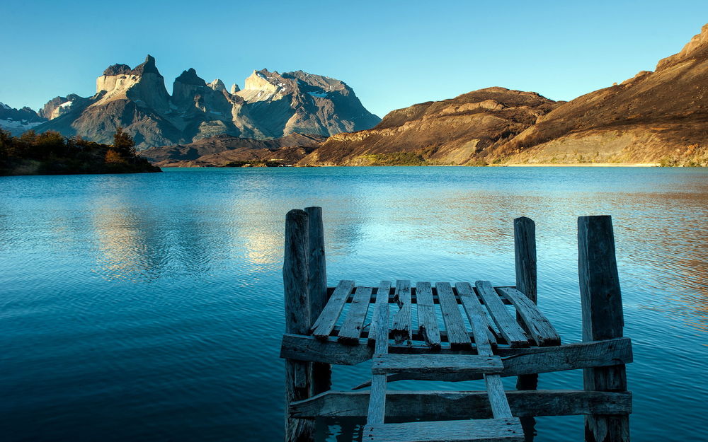 Обои для рабочего стола Деревянный причал, стоящий у берега горного озера на фоне безоблачного неба