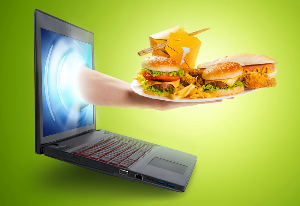 Обои для рабочего стола Рука с экрана ноутбука подает тарелку с гамбургерами и другими продуктами Макдональдса