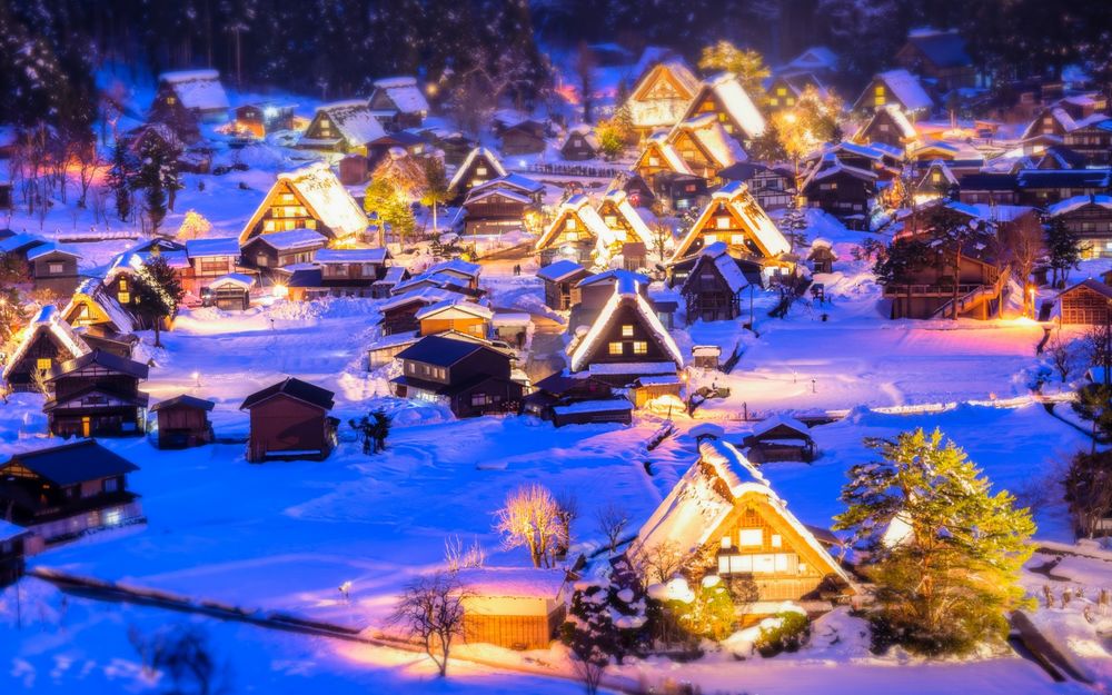 Обои для рабочего стола Заснеженный коттеджный поселок с ярко освещенными домами в окружении деревьев, готовится к встрече новогодних и рождественских праздников