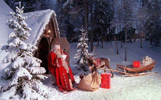 Обои на рабочий стол Санта Клаус / Santa Claus сидит возле своей хижины и читает письмо, рядом мешок с подарками и упряжка с оленем