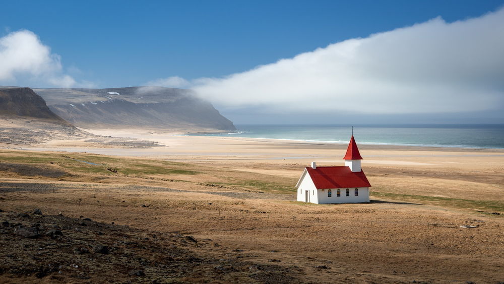 Обои для рабочего стола Небольшая, каменная церковь, стоящая на океанском, скалистом побережье на фоне синего неба с белыми, кучевыми облаками