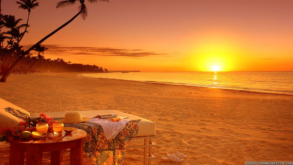 Обои для рабочего стола На побережье моря в лучах заходящего солнца, стоит лежак и столик с двумя стаканами сока
