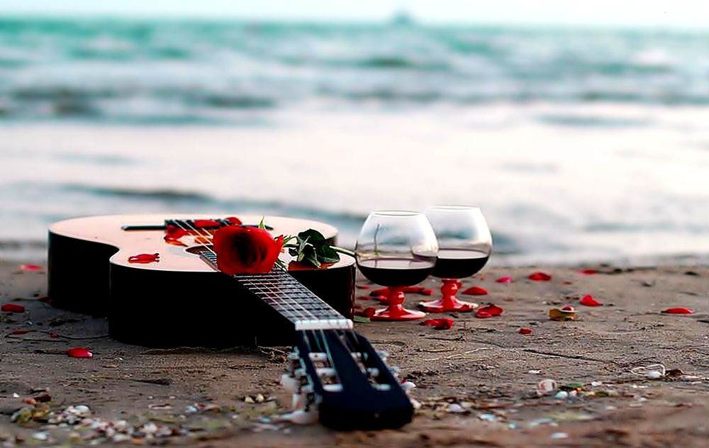 Обои для рабочего стола На берегу моря лежит гитара, стоят два бокала вина и красная роза, шумит прибой