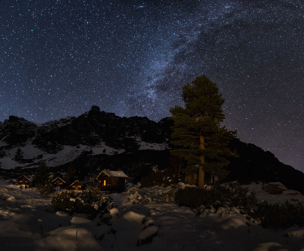 Обои для рабочего стола Небольшой поселок, стоящий на заснеженном предгорье на фоне ночного, звездного неба и Млечного пути, автор Емил Рашковски