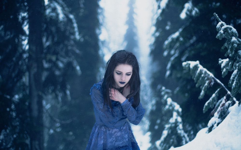 Обои для рабочего стола Девушка с готическим макияжем одетая в легкое платье стоит в зимнем лесу приложив руки к груди