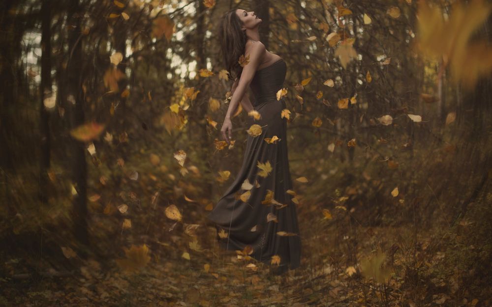Обои для рабочего стола Девушка стоит на поляне, в лесу в окружении падающих осенних листьев