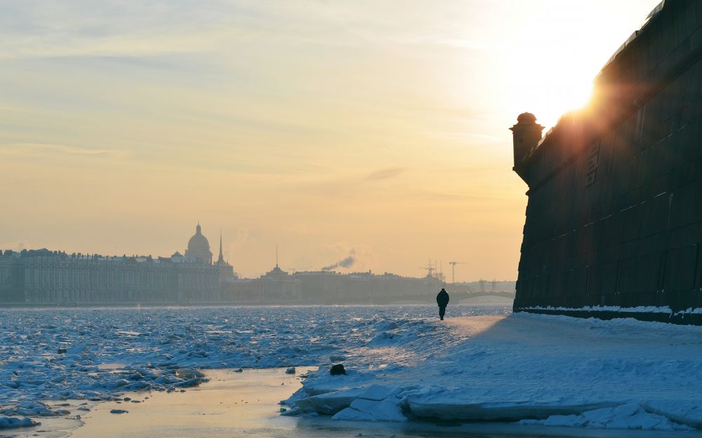 Обои для рабочего стола Одинокий мужчина, идущий по заснеженному берегу Невы возле каменной пристани на фоне восхода солнца на утреннем, пасмурном небосклоне, Санкт-Петербург, Россия / Neva, St. Petersburg, Russia