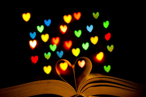 Обои на рабочий стол Из раскрытой книги, где средние листы образуют форму сердца, поднимаются вверх разноцветные светящиеся сердечки