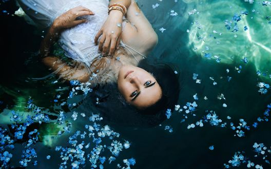 Обои на рабочий стол Темноволосая голубоглазая девушка плавающая в воде среди голубых лепестков