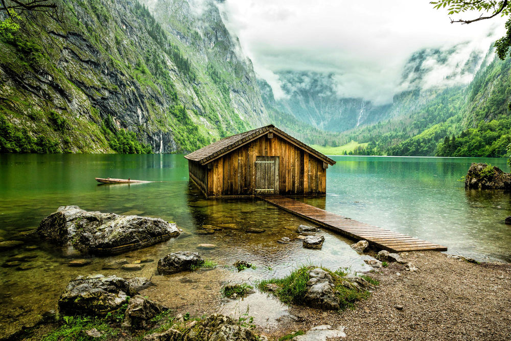 Обои для рабочего стола Деревянный, рыбацкий домик, стоящий на мелководье горного озера с молочным туманом, опускающимся с горных вершин