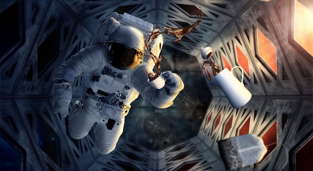 Обои для рабочего стола Космонавт в скафандре летает в невесомости внутри космического корабля, держит в руке чашку пытаясь попить чая. Рядом летает кувшин с чаем и пакетик с заваркой чая