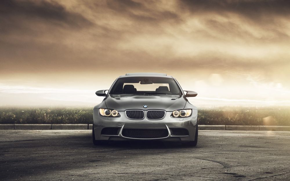 Обои для рабочего стола Автомобиль BMW 335i на парковке на фоне облачного неба. Вид спереди