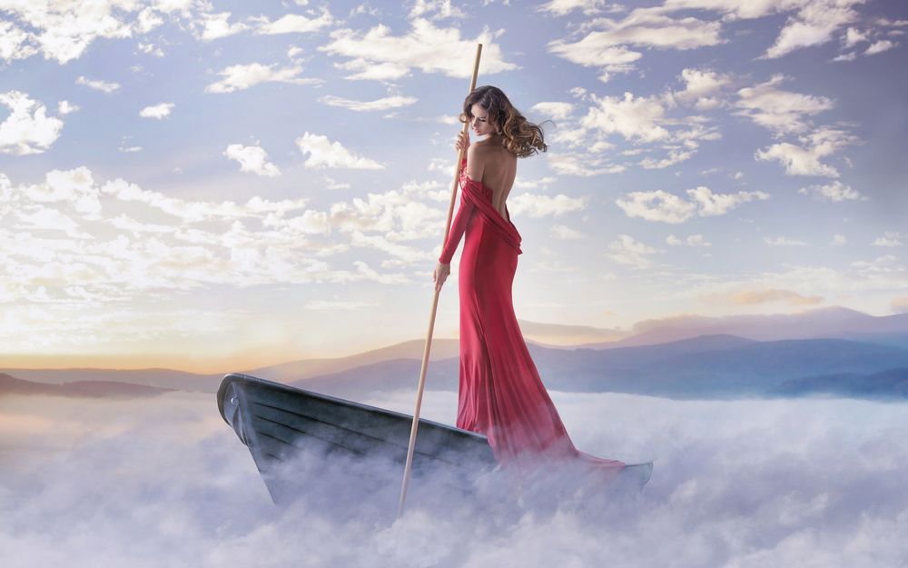 Обои для рабочего стола Девушка в красном платье стоит в лодке плывущей по озеру в окружении тумана