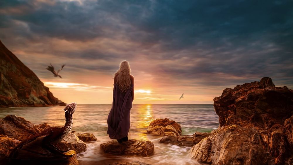 Обои для рабочего стола Дейенерис Таргариен / Daenerys Targaryen стоит на берегу моря, глядя на закат солнца, возле нее лежит и парят в небе ее драконы