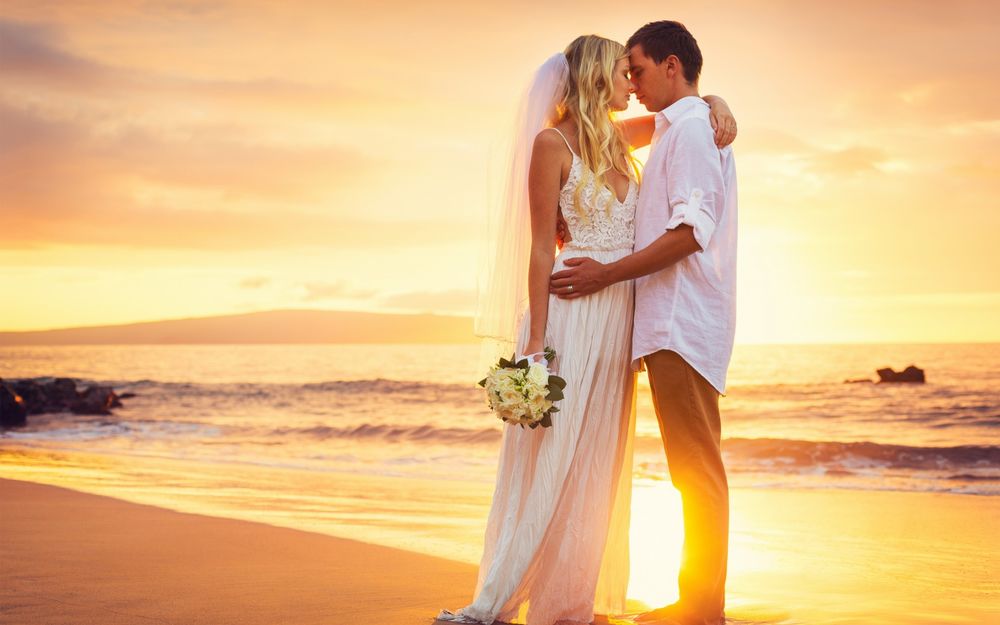 Обои для рабочего стола Жених и невеста с букетиком цветов в руке, стоят обнявшись на берегу моря
