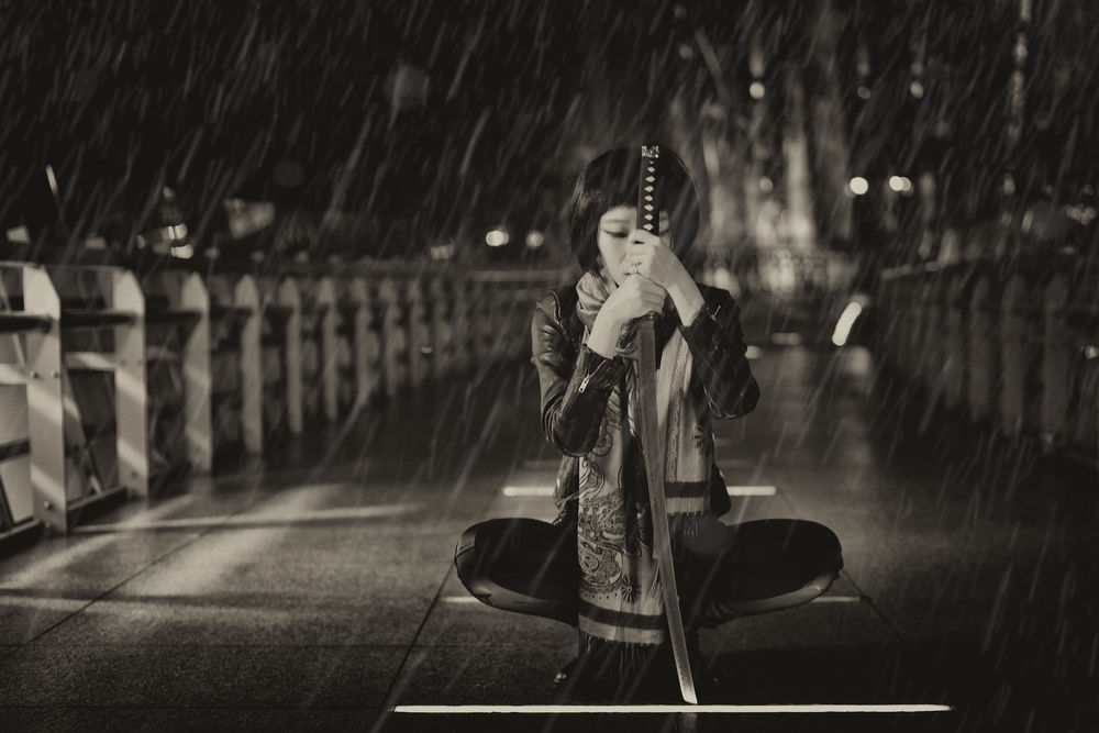 Обои для рабочего стола Девушка азиатской внешности, сидит на мосту с катаной в руках под проливным дождем