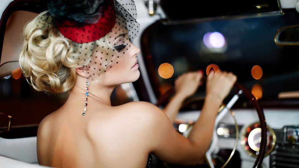 Обои для рабочего стола Модель Екатерина Коба в вечернем наряде, в шляпке с вуалью за рулем авто, за окошком размытый фон ночного города