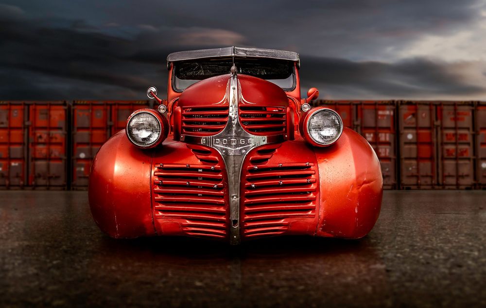 Обои для рабочего стола Красный легковой ретро автомобиль Dodge стоит на площадке, перед контейнерами