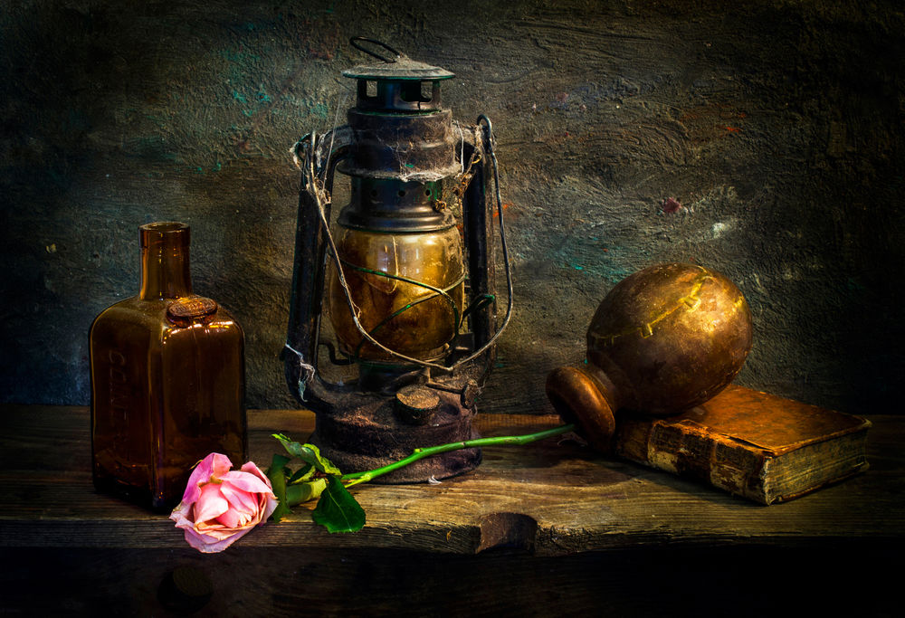 Обои для рабочего стола Керосиновая лампа, стеклянная бутылка, книга, опрокинутый кувшин и розовая роза лежат на деревянной доске