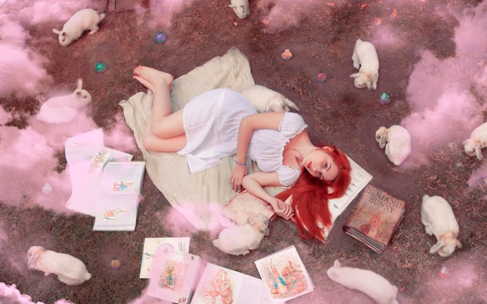Обои для рабочего стола Красноволосая девушка лежит на земле среди книг и розового дыма, рядом сидят белые кролики