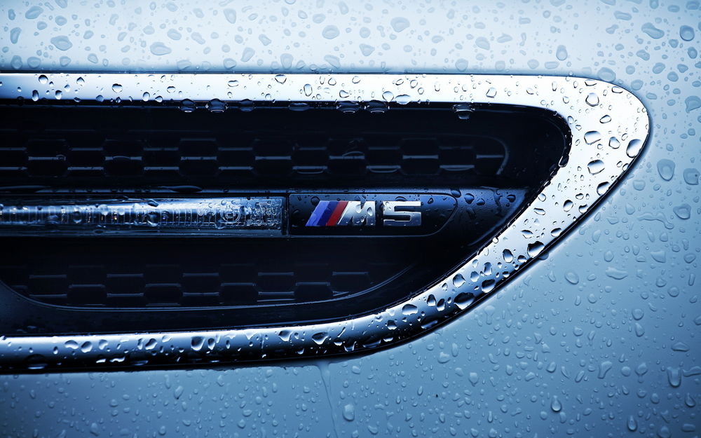 Обои для рабочего стола Шильдик фирмы BMW M5 на крыле авто, в каплях воды