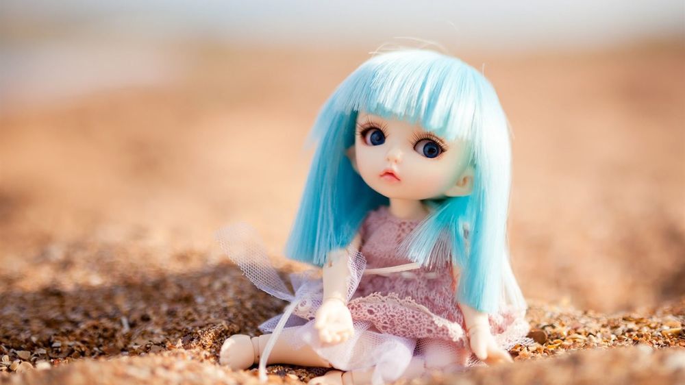 Обои для рабочего стола Кукла с голубыми волосами сидит на песке