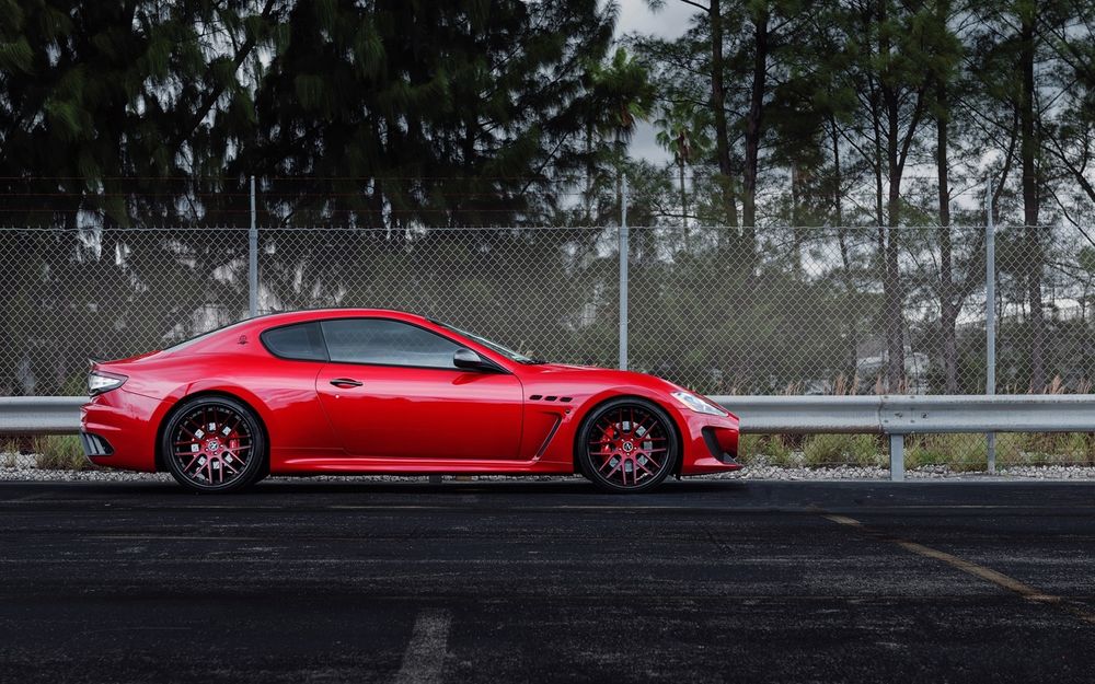 Обои для рабочего стола Maserati Granturismo на огражденной трассе на фоне деревьев