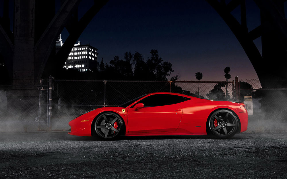 Обои для рабочего стола Ferrari на огражденной площадке на фоне ночного неба, дома и деревьев
