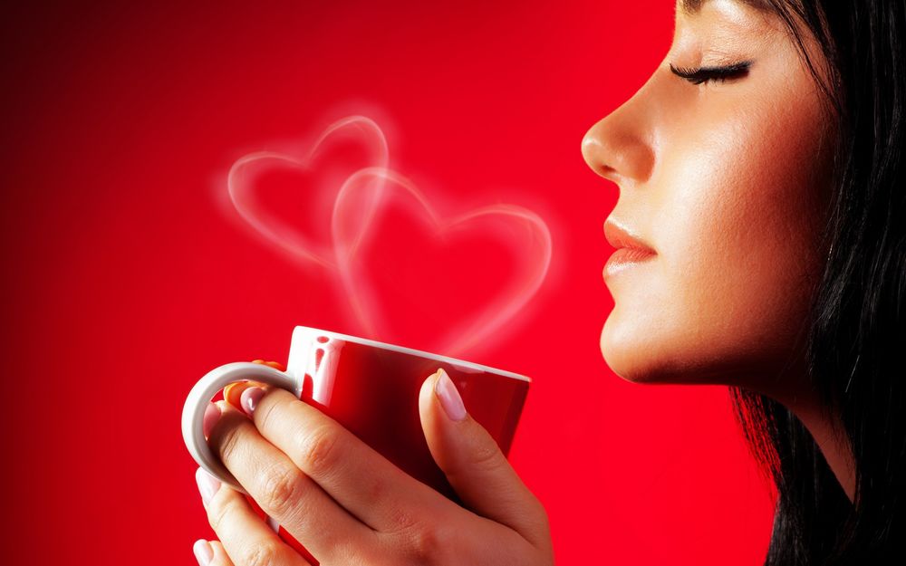 Обои для рабочего стола Девушка держит в руках красную кружку с горячим напитком от которой исходит пар в виде двух сердечек