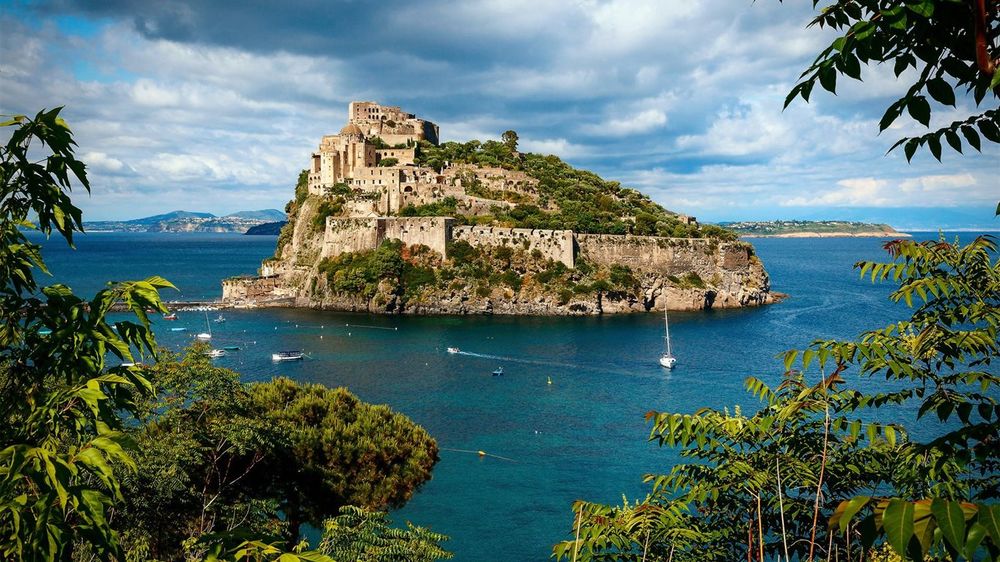 Обои для рабочего стола Арагонский замок-крепость на острове Искья в Италии, на фоне воды, неба и деревьев