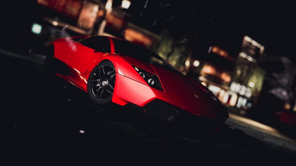 Обои для рабочего стола Красное авто lamborghini на размытом темном фоне города