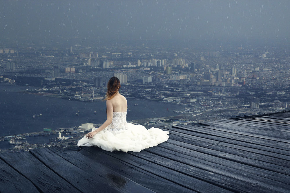 Обои для рабочего стола Девушка сидит на крыше под дожем с видом на город