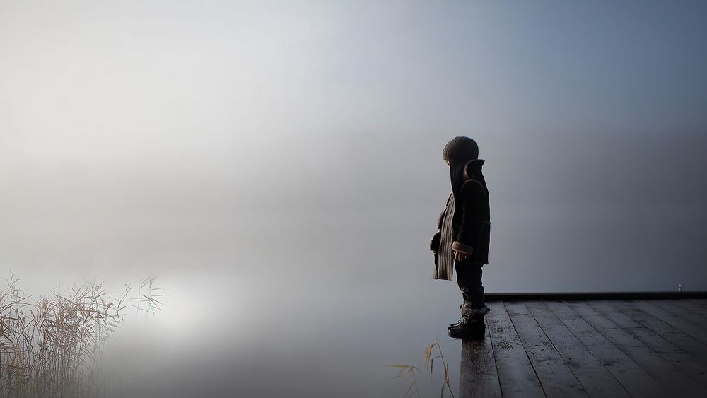 Обои для рабочего стола Мальчик стоит у озера на деревянном мостике в густом тумане
