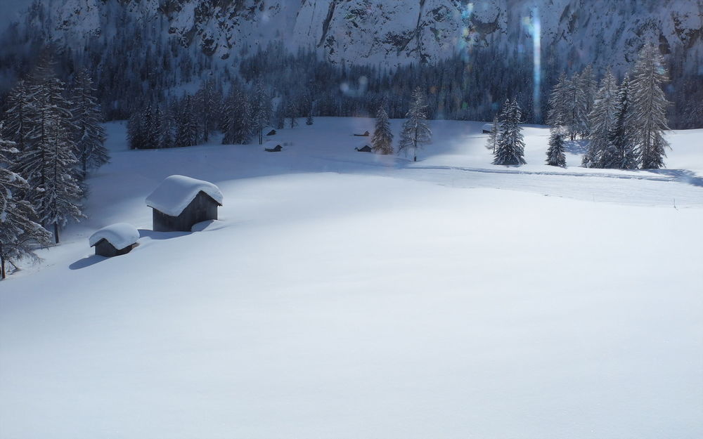 Обои для рабочего стола Покрытые снегом крыши домов и деревья на фоне гор