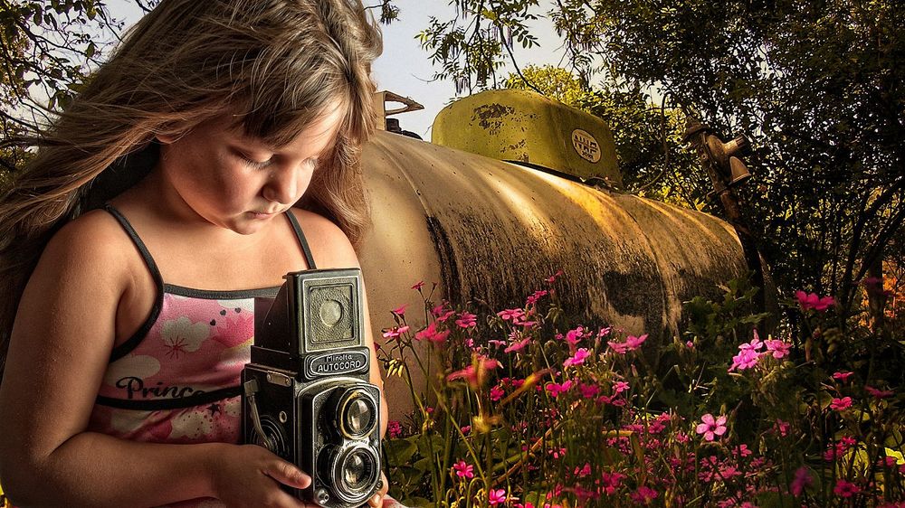 Обои для рабочего стола Девочка держа в руках фотоаппарат фотографирует природу, стоя у огромной металлической бочки