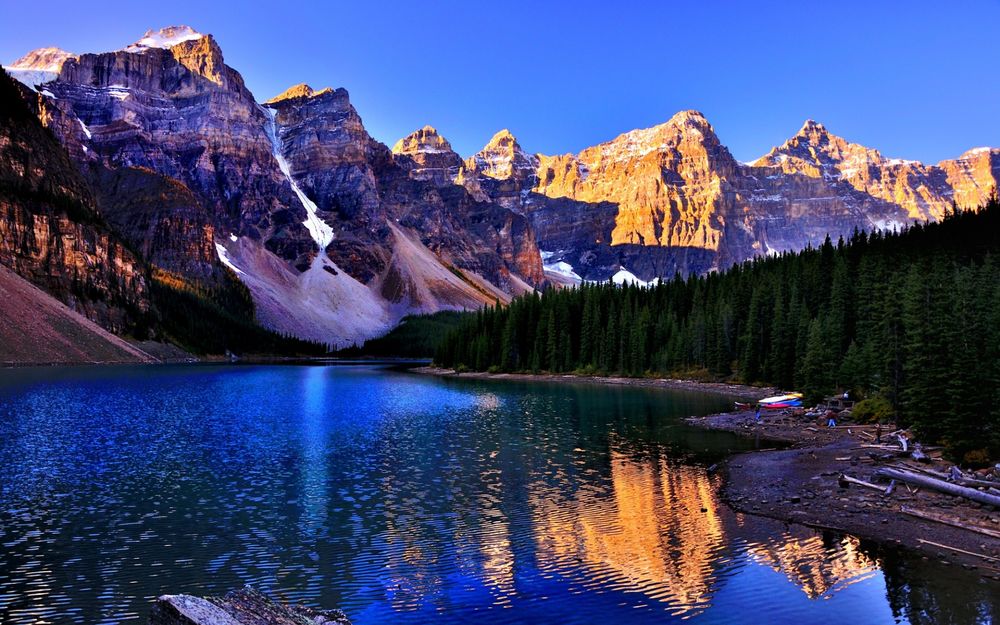 Обои для рабочего стола Озеро с берегами, покрытыми высокими елями, окруженное горами с заснеженными пиками на фоне ярко-голубого, безоблачного неба