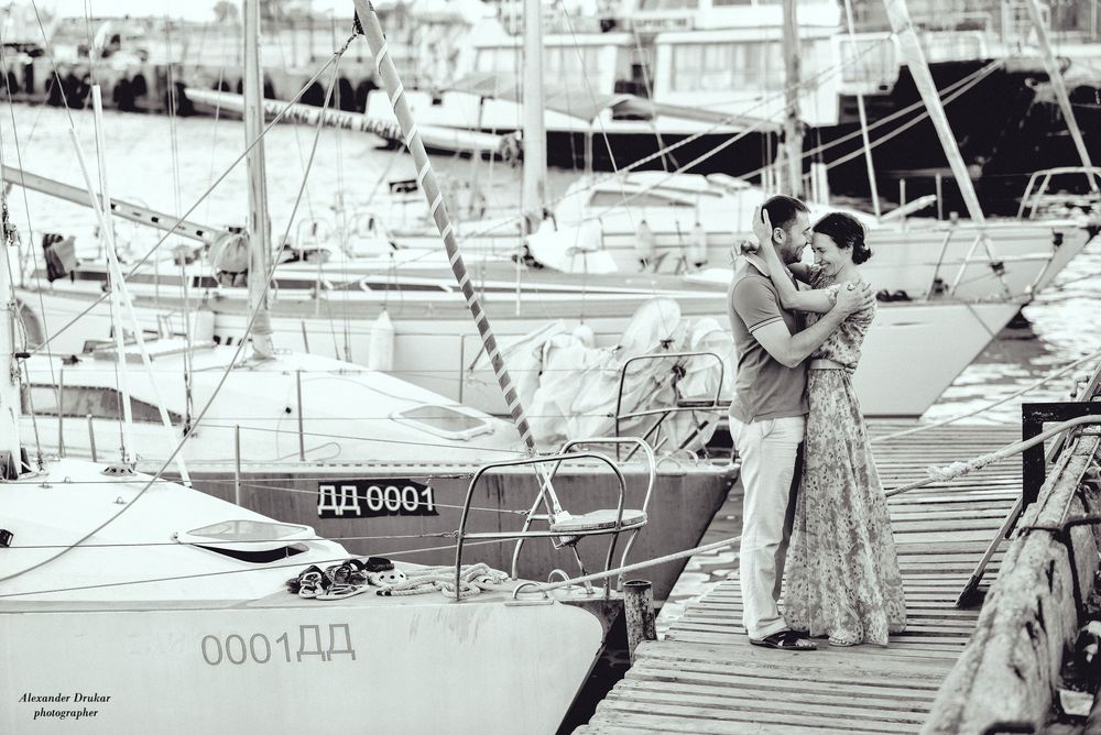 Обои для рабочего стола Парень и девушка улыбаются и обнимаются, стоя на пирсе, рядом с пирсом много яхт, фотограф Александр Друкар