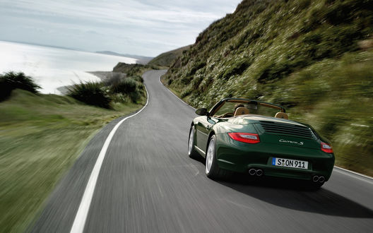 Обои на рабочий стол Porsche Carrera S мчится по дороге вдоль горы