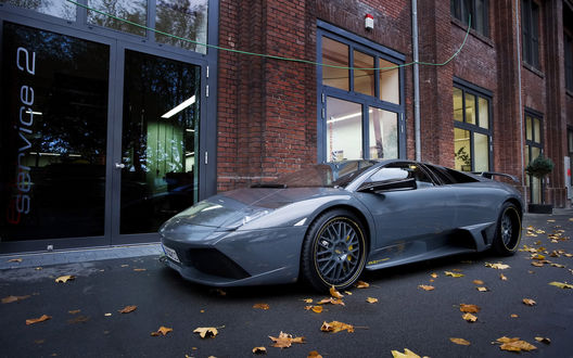Обои на рабочий стол Автомобиль марки Lamborghini припаркованный рядом с домом, на дороге опавшие клиновые листья