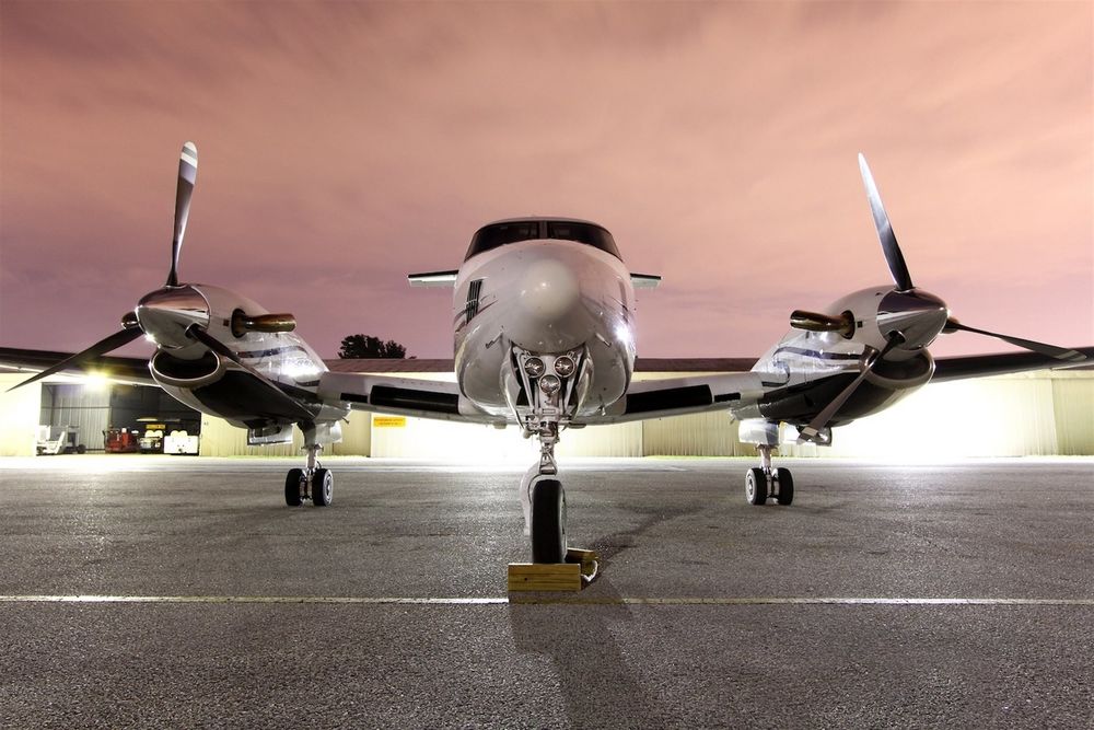 Обои для рабочего стола На взлетной полосе аэродрома стоит моторный самолет, King Air200 на фоне подсветки и вечернего неба