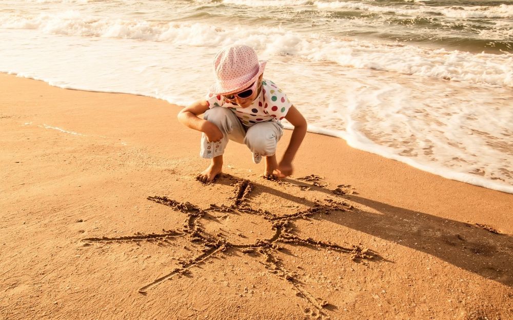Обои для рабочего стола На берегу моря, ребенок на песке нарисовал солнце