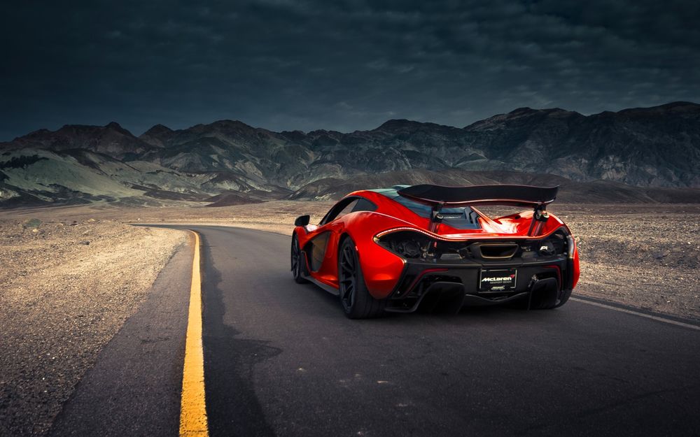 Обои для рабочего стола Красный Hypercar едет по дороге в направлении гор