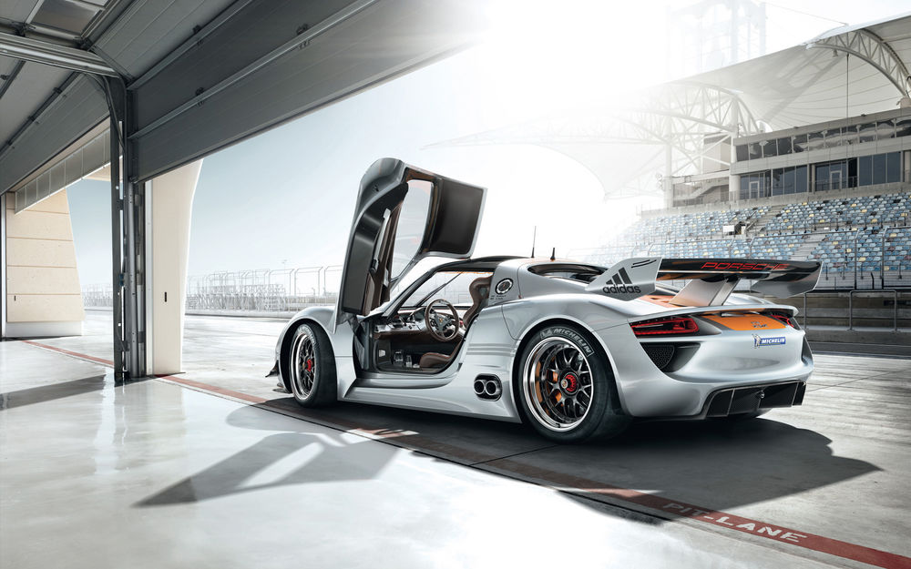 Обои для рабочего стола Белый автомобиль Porshe 918 rsr, concept car стоит на дороге, а рядом находится здание и трибуна