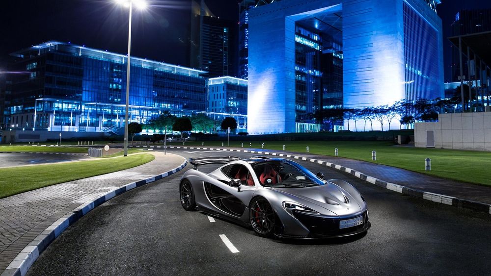 Обои для рабочего стола Суперкар McLaren P1 серого цвета, стоит посередине дороги, при свете уличного фонаря, на заднем плане деревья и дома