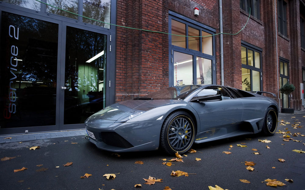 Обои для рабочего стола Автомобиль марки Lamborghini припаркованный рядом с домом, на дороге опавшие клиновые листья