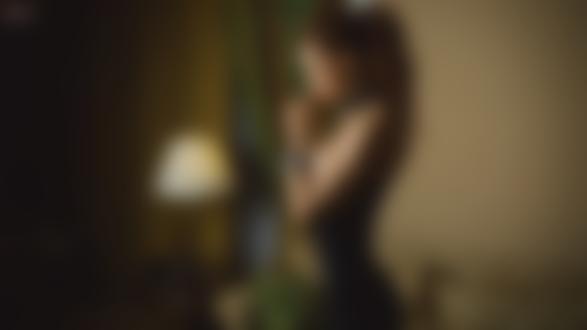 Обои на рабочий стол Девушка прикасаясь руками к губам, стоит в зеленом платье в комнате