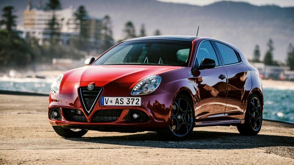 Обои на рабочий стол Автомобиль марки Alfa Romeo Giulietta стоит на пирсе на фоне города