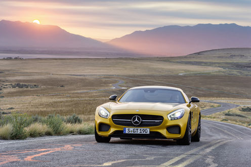 Обои на рабочий стол Желтый автомобиль марки Mercedes-Benz AMG GT S, стоит на дороге на фоне гор, освещаемых солнцем на закате